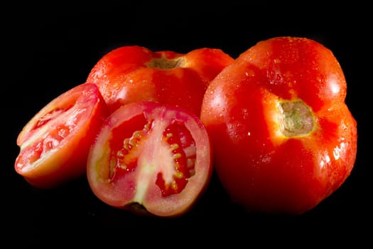 Close up view of a bunch of red tomatoes isolated on a black background.