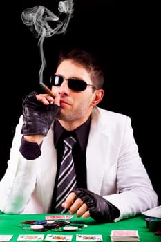 View of a gangster man playing some cards and poker, smoking a Cuban cigar.