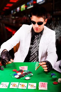 View of a gangster man playing some cards and poker, smoking a Cuban cigar.
