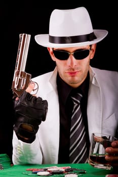 View of a gangster man playing some cards and poker, holding a gun.