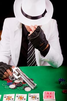 View of a gangster man playing some cards and poker, holding a gun.