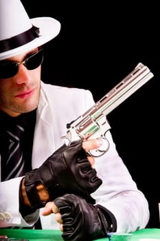 View of a gangster man playing some cards and poker,  holding a gun.