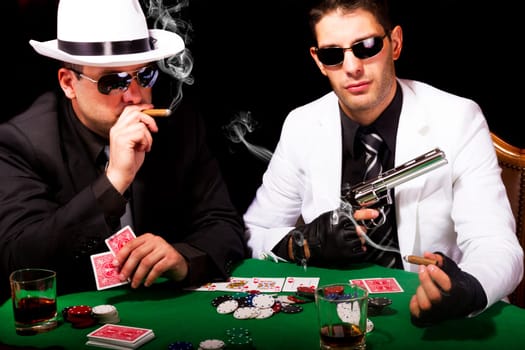 View of two gangster males playing some poker and smoking Cuban cigars.