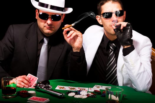 View of two gangster males playing some poker and smoking Cuban cigars.
