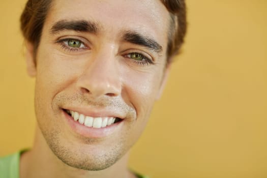 portrait of caucasian college student smiling and looking at camera with yellow wall in background. Selective focus, copy space