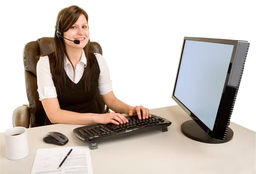 An attractive smiling businesswoman is wearing a headset and looking at the camera from her desk.