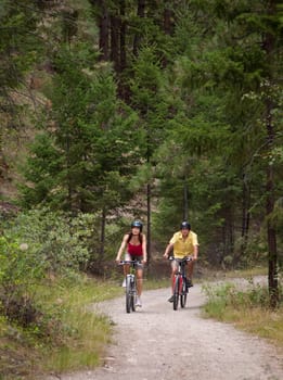 Outdoor photo of young adult couple riding bicycles on forest trail.