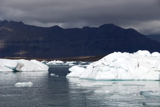 Iceberg reflections on the calm water of the lake Jokulsarlon with black mountains