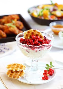 White yogurt with caramelized berries with chicken wings and vegetable salad in background