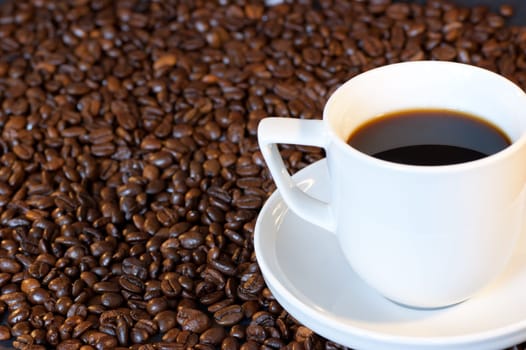 A cup of coffee surrounded by roasted coffee beans