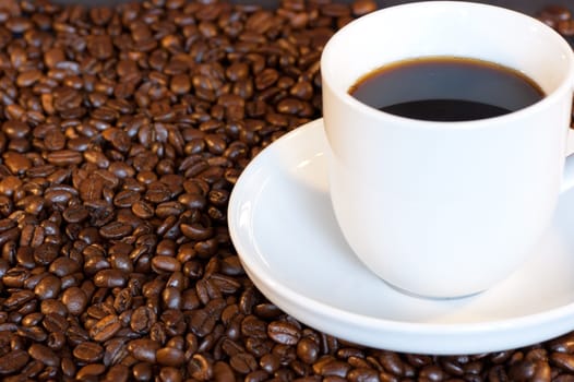 A white cup and saucer filled with black coffee among roasted coffee beans