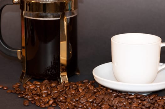A jug of coffee with a white cup and saucer among coffee beans