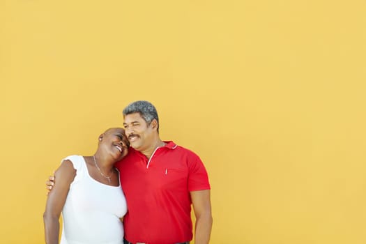 mature latin american couple hugging and smiling with yellow wall in background. Waist up, copy space