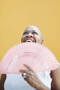 portrait of african 50 years old woman with bald head smiling on yellow background and looking up. Head and shoulders, copy space