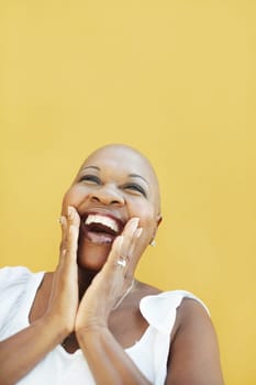 portrait of african 50 years old surprised woman with bald head, smiling on yellow background. Head and shoulders, copy space