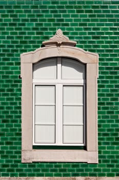 Traditional stone decorated window in a green tile background, Algarve, Portugal
