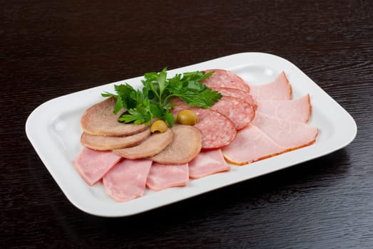 Meat assortment of beef tongue, sausage, meat and ham with greens