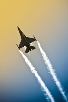 aerobatic military jet in a gradient sky leaving a smoke trail