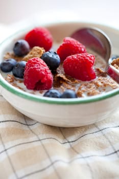 Bowl of cereal with raspberries, blueberries and milk for healthy breakfast.