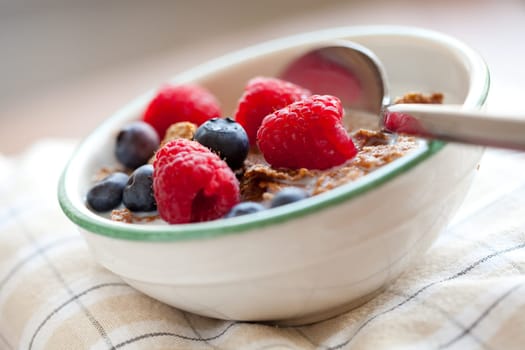 Bowl of cereal with raspberries, blueberries and milk for healthy breakfast.