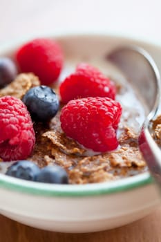 Bowl of cereal with raspberries, blueberries and milk for healthy breakfast.