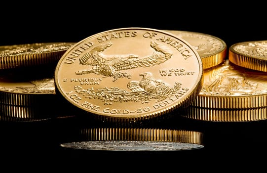 Close up of a solid gold eagle one ounce coin stacked on other coins and reflected in black surface