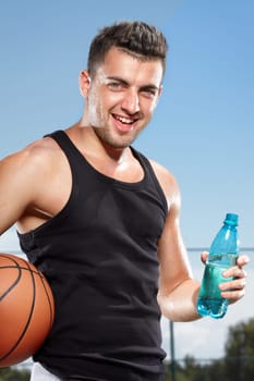 Young thirsty man drinking water on sports field