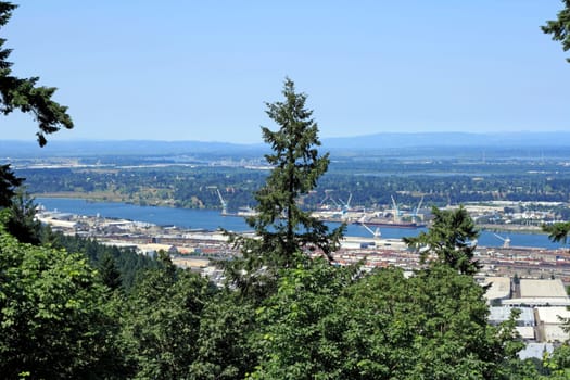 View overlooking north Portland, Oregon industrial river district with lots of trains, cranes, warehouses and ships during a summer day.