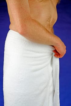 Nude man in front of a dark blue background wrapping a white towel around his waist after a healthy shower.