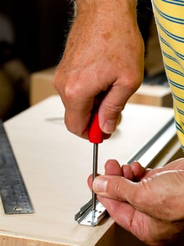 Screwing a screw into a drawer runner on side of wooden drawer