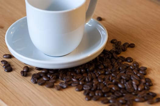 White cup and saucer with coffee beans on an oak table top