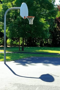 Basketball court outdoor early morning summer sun in a public park surrounded by trees.