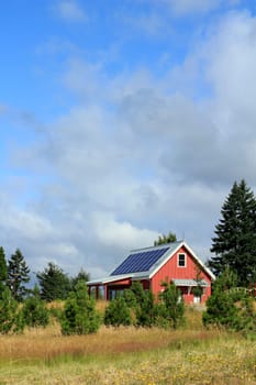 Small, red public park building with solar panels on the metal rooftop on a mostly sunny summer day.