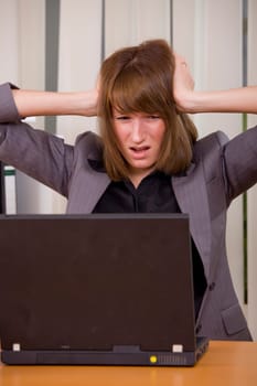 stressed businesswoman holding her head with both hands looking at laptop
