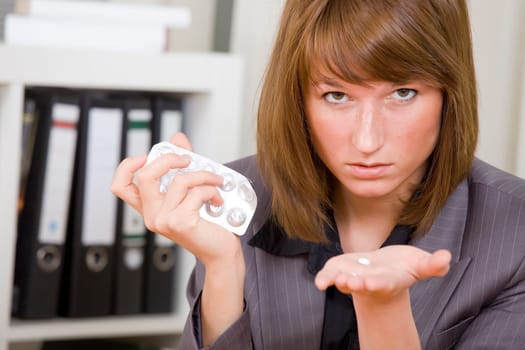 stressed businesswoman holding pills in her hand in office