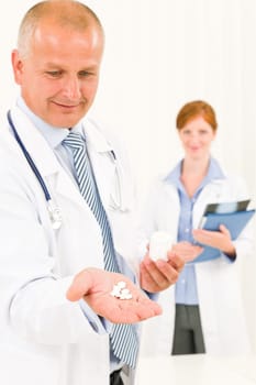 Medical doctor team senior male holding pills young female colleague