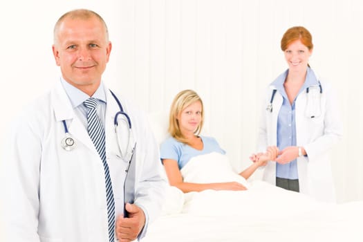 Two medical doctors with patient lying in bed examine pulse