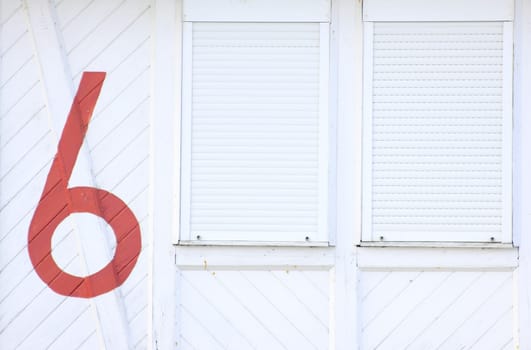 white wooden wall with two closed windows and the inscription with the number six