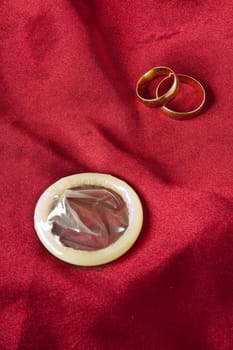 Wedding ring on the condom against the red satin