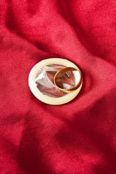 Wedding ring on the condom against the red satin