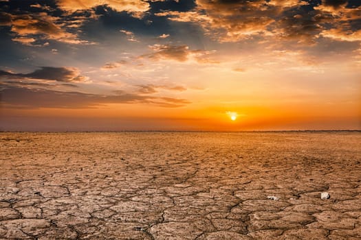 Global worming concept - cracked scorched earth soil drought desert landscape dramatic sunset