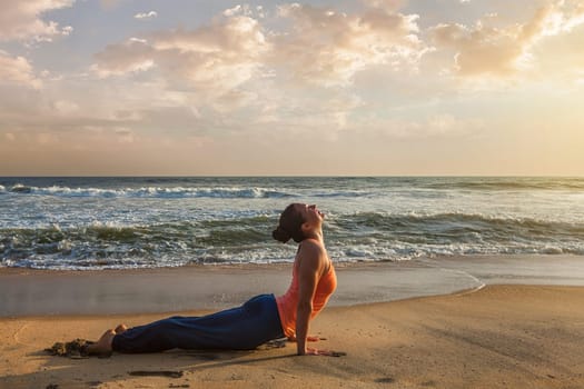 Yoga outdoors on beach - woman practices Ashtanga Vinyasa yoga Surya Namaskar Sun Salutation asana Urdhva Mukha Svanasana - upward facing dog pose on sunset. Kerala, India