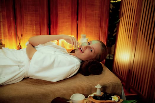 Serene ambiance of spa salon, woman customer smiling and rejuvenating with luxurious face cream massage with warm lighting candle. Facial skin treatment and beauty care concept. Quiescent
