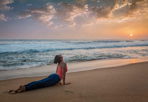 Yoga outdoors on beach - woman practices Ashtanga Vinyasa yoga Surya Namaskar Sun Salutation asana Urdhva Mukha Svanasana - upward facing dog pose on sunset. Kerala, India