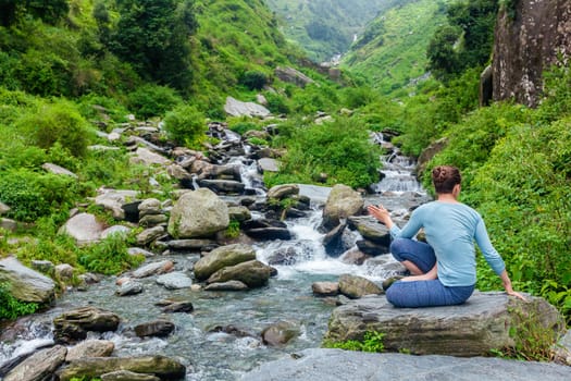 Yoga exercise outdoors - woman doing Ashtanga Vinyasa Yoga asana Marichyasana D seated spinal twist pose at waterfall in mountains