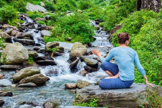 Yoga exercise outdoors - woman doing Ashtanga Vinyasa Yoga asana Marichyasana D seated spinal twist pose at waterfall in mountains