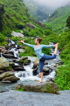 Yoga outdoors - woman doing yoga asana Natarajasana - Lord of the dance balance pose outdoors at waterfall in Himalayas