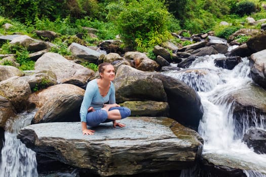 Yoga exercise outdoors - woman doing Ashtanga Vinyasa Yoga arm balance strength training asana Tolasana - scales pose at waterfall in Himalayas