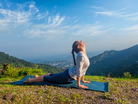 Yoga outdoors - woman practices Ashtanga Vinyasa yoga Surya Namaskar Sun Salutation asana Urdhva Mukha Svanasana - upward facing dog pose in mountains in the morning