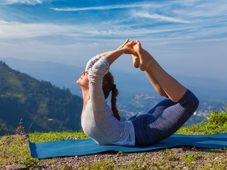 Yoga outdoors - young sporty fit woman doing Ashtanga Vinyasa Yoga asana Dhanurasana - bow pose - in Himalayas mountains in the morning Himachal Pradesh, India